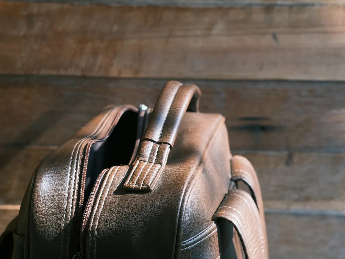 Close-up of a brown leather backpack handle and zippers against wooden boards.