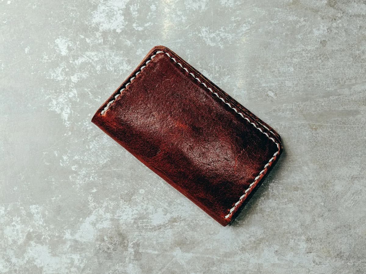 Closed brown leather wallet with light edge stitching on a concrete surface.