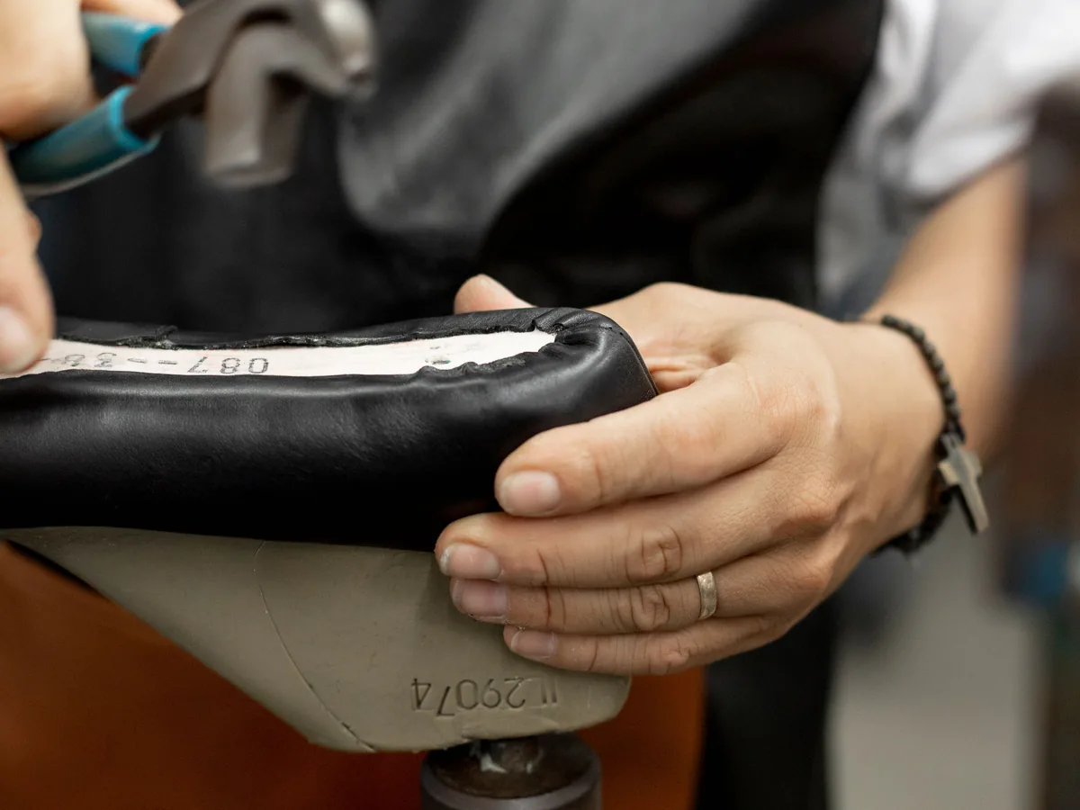 Hands working on a black shoe mounted on a shoemaking last.